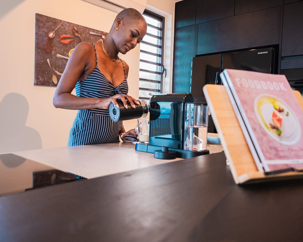 A person using a coffee machine in a modern kitchen with a book on the counter.
