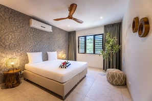 A bedroom with a large bed, a ceiling fan, an air conditioning unit, a bedside lamp, a window with curtains, and a potted plant. - Luxury penthouse with panoramic sea views (Sint Willibrordus)