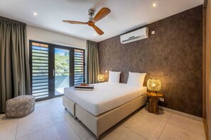 Ein modernes Schlafzimmer mit einem großen Bett, einem Deckenventilator und Blick auf Grün durch das Fenster.