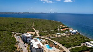 An aerial view of a coastal property with modern buildings, a swimming pool, and a clear view of the sea. - Luxury penthouse with panoramic sea views - Coral Estate (Sint Willibrordus)
