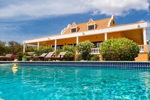 Un hôtel doté d’une piscine, d’un espace extérieur couvert avec des chaises longues, et d’un bâtiment avec un toit en tuiles.
