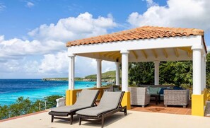 Un espace extérieur aménagé, abrité et doté de fauteuils et d’une table, offrant une vue sur la côte.