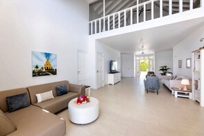 Amplia sala de estar con techo alto, balcón, un conjunto de sofás, una mesa redonda con flores y un cuadro de un edificio en la pared.