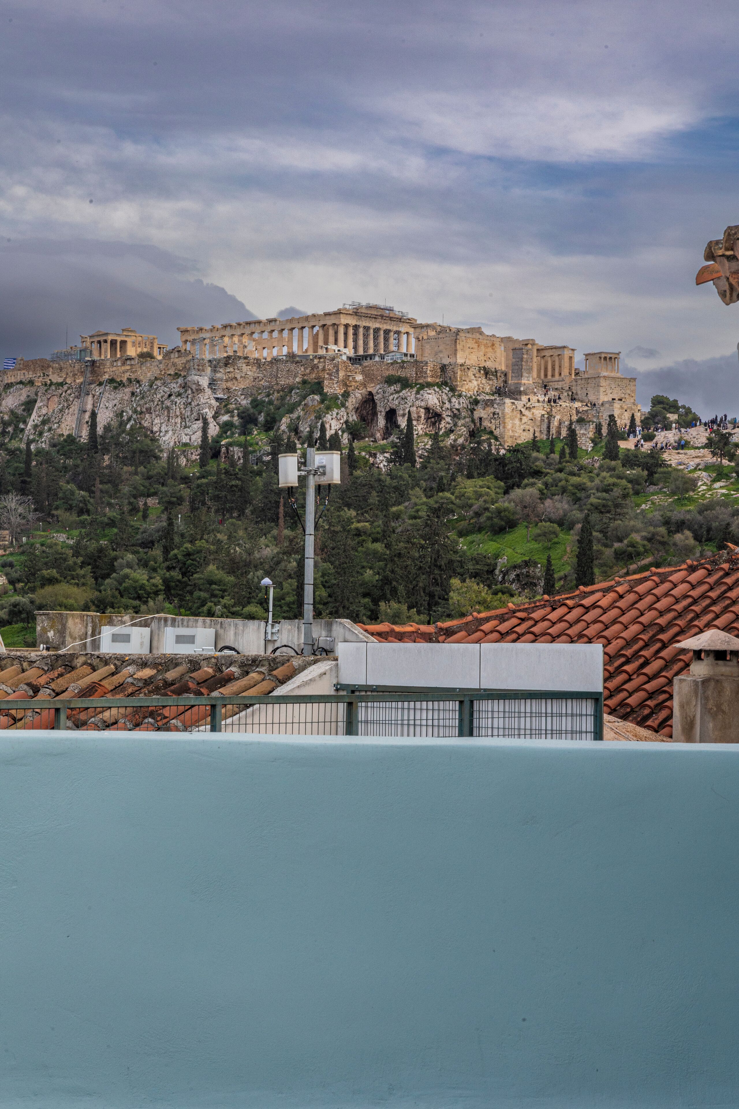 A view of ancient ruins atop a hill with modern buildings in the foreground.