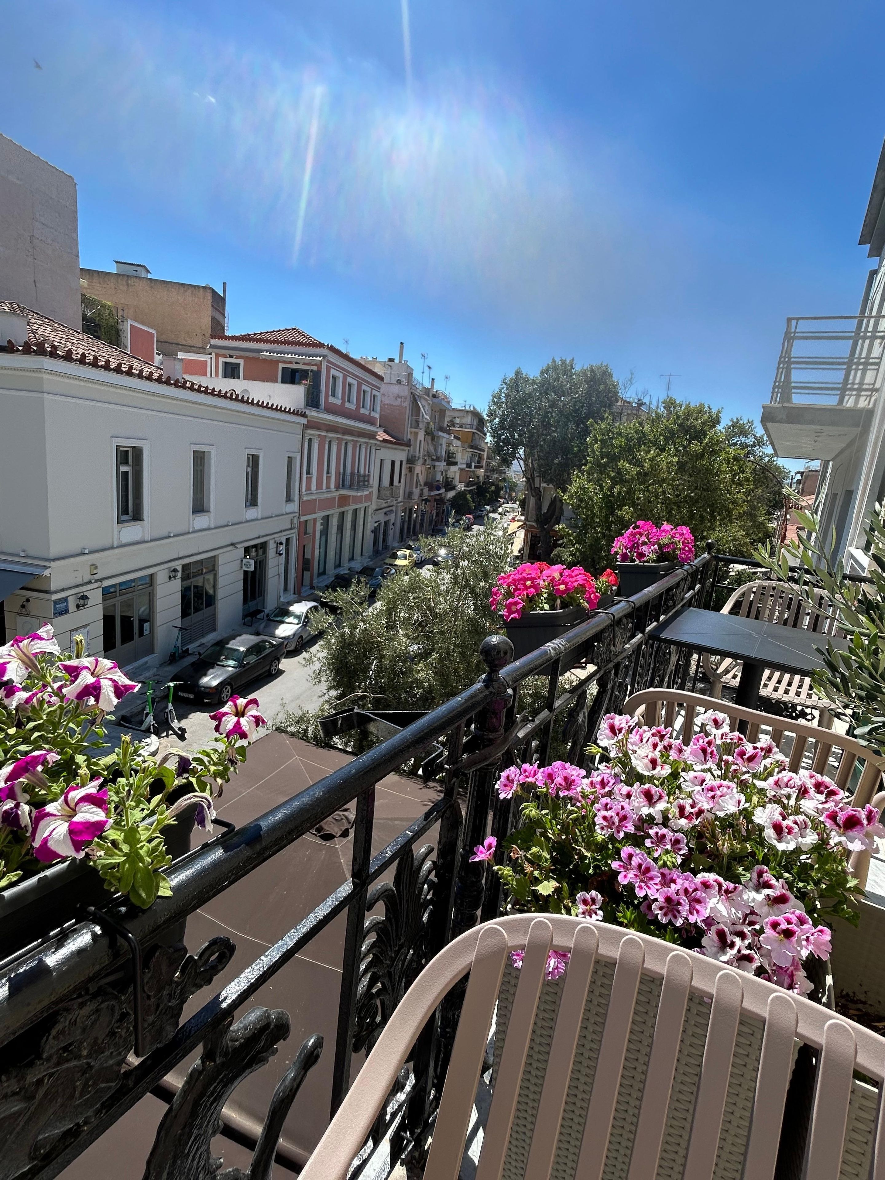 A balcony with a view of a street lined with buildings, a chair, and potted flowers.