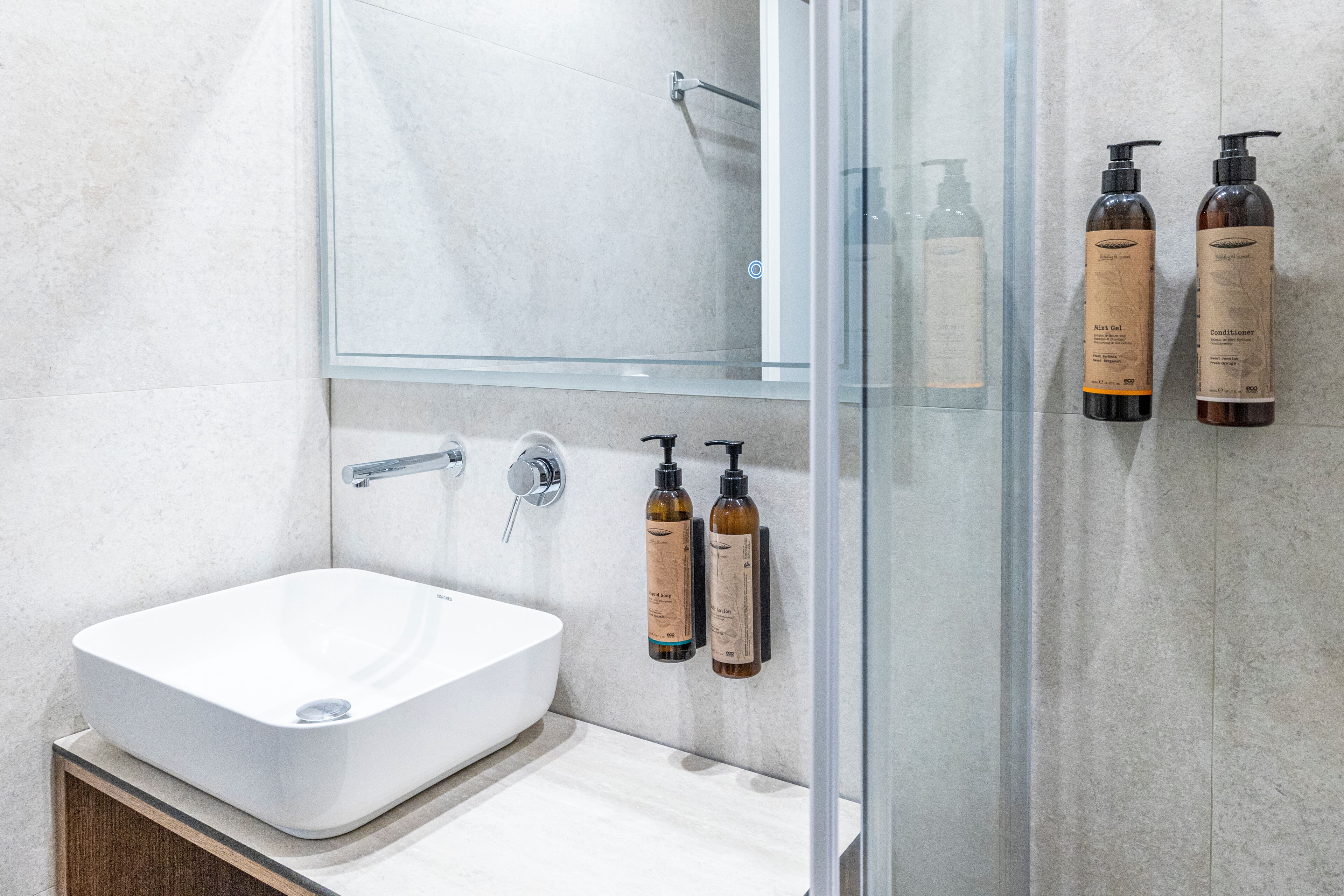 A modern bathroom with a white sink, a glass shower enclosure, and two bottles of lotion on the wall.