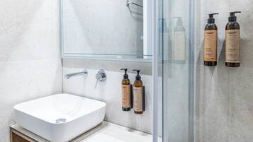 A modern bathroom with a white sink, a glass shower enclosure, and two bottles of lotion on the wall.