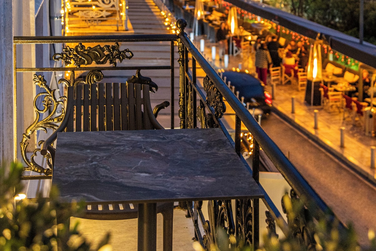 A balcony with a view of a street at dusk, featuring a railing, a bench, and a table.