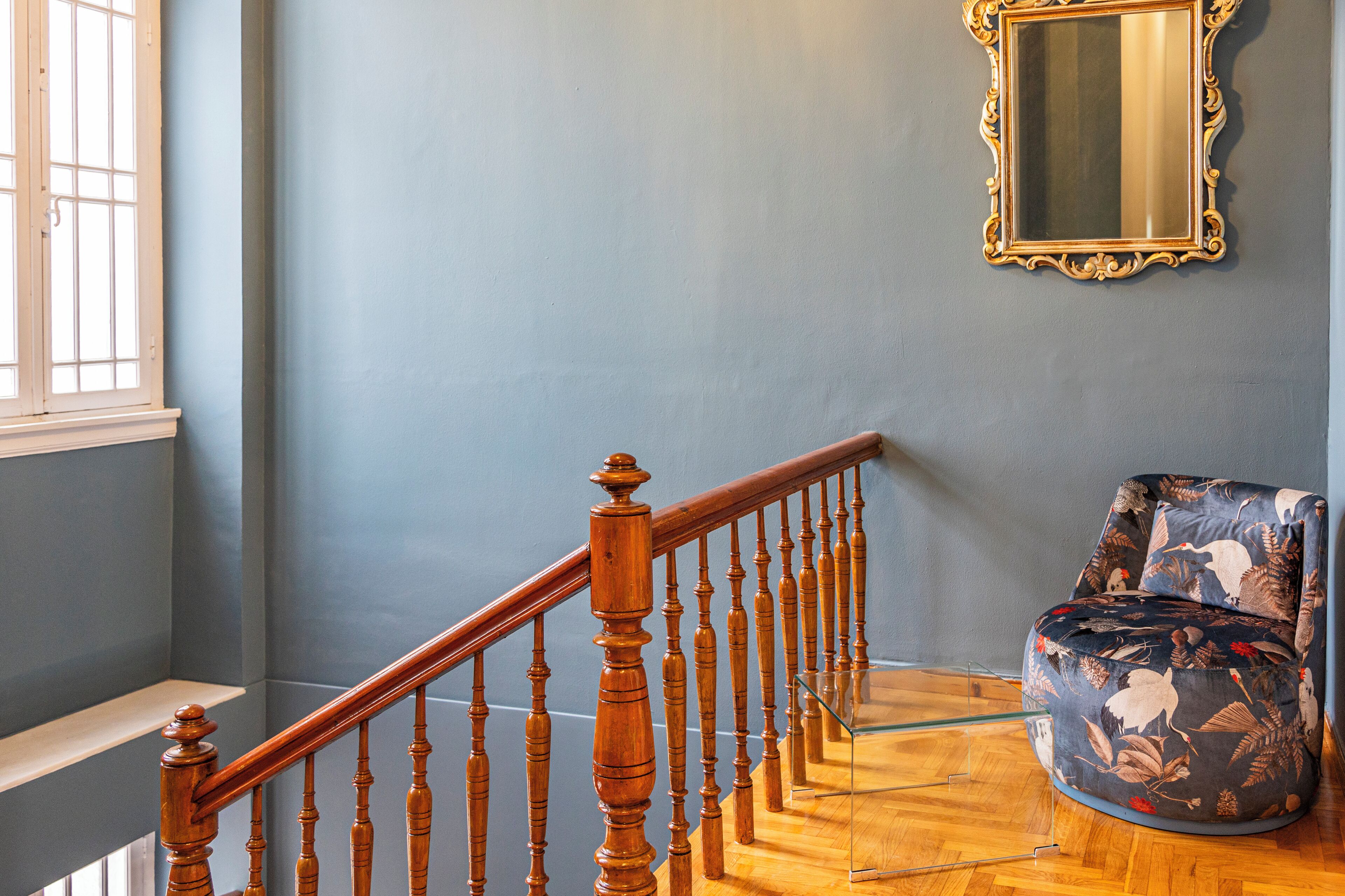 A staircase with wooden balusters, a chair with a floral pattern, and a mirror on the wall.