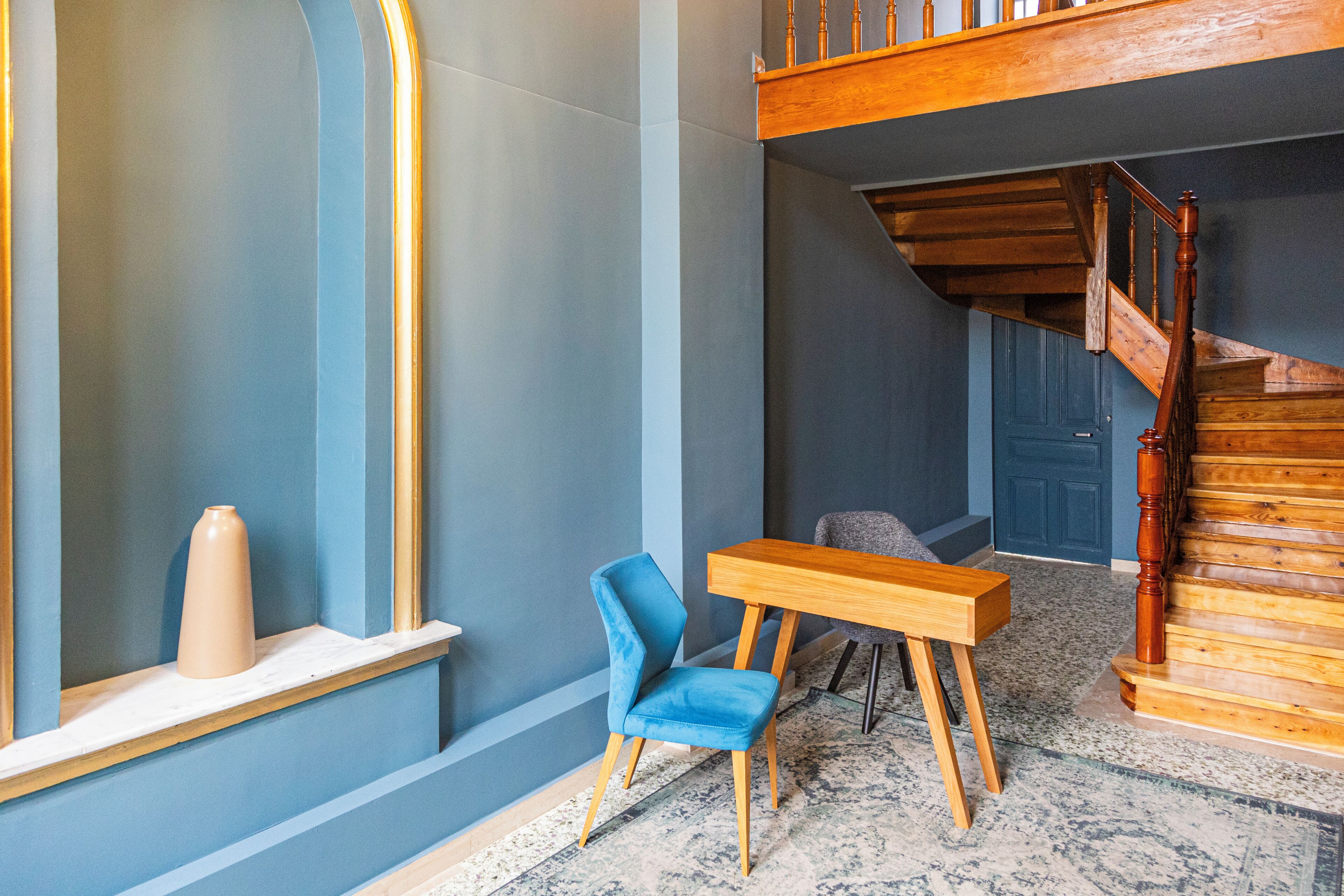A modern interior with a blue wall, a wooden staircase, a blue chair, and a wooden table.