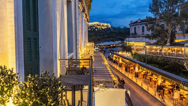A terrace with outdoor seating, overlooking a street with shops and a hill in the background. - Iliotropio Athens, Thisio (Athens)
