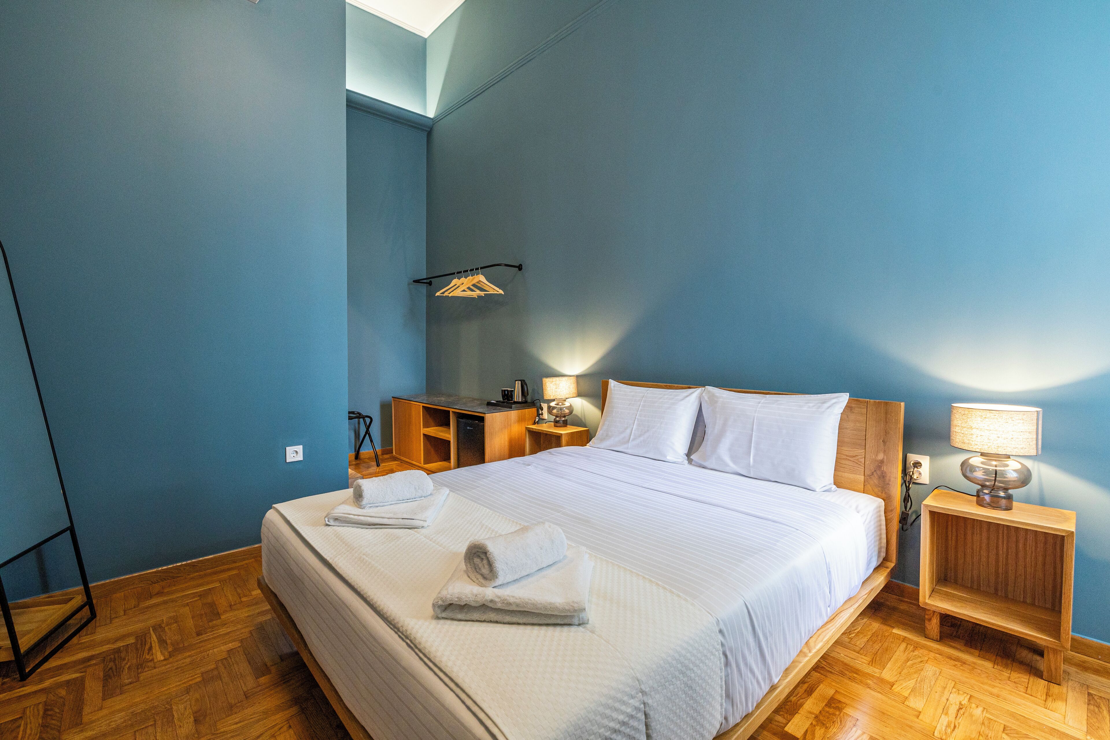 Un lit bien fait, avec deux serviettes, une table de chevet avec une lampe et un petit bureau avec une chaise.