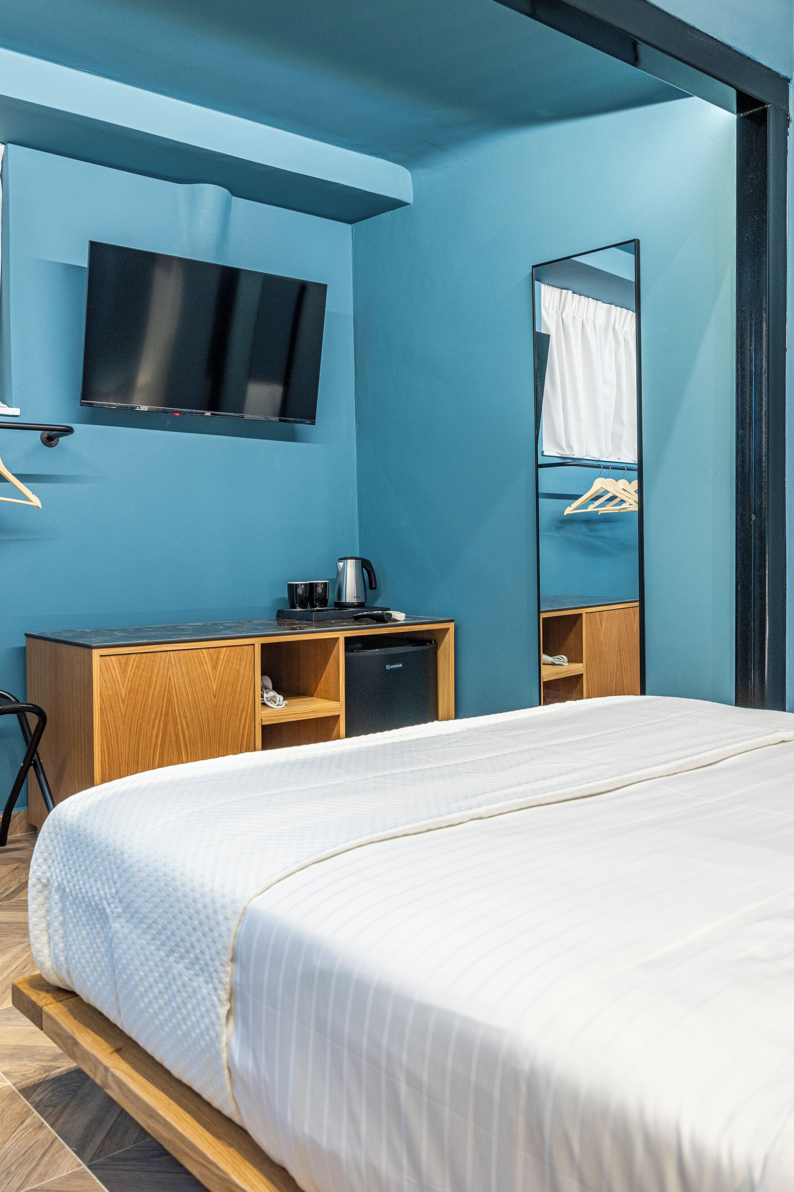 Ein modernes Hotelzimmer mit einem großen Bett, einem Flachbildfernseher an der Wand, einem Holztisch mit Kaffeemaschine und einem eingebauten Kleiderschrank.