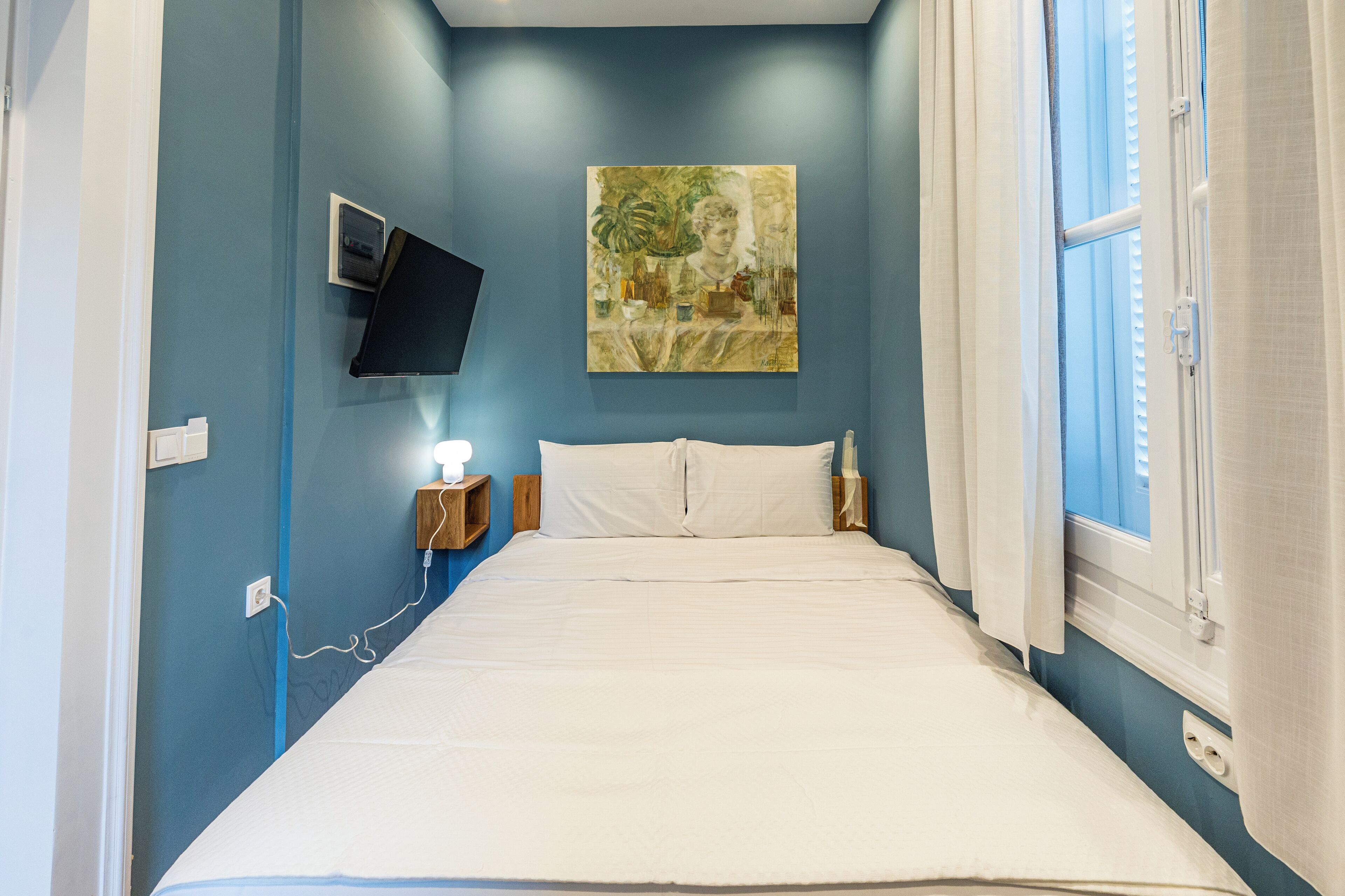 A bedroom with a bed, a wall-mounted TV, and a window with curtains.