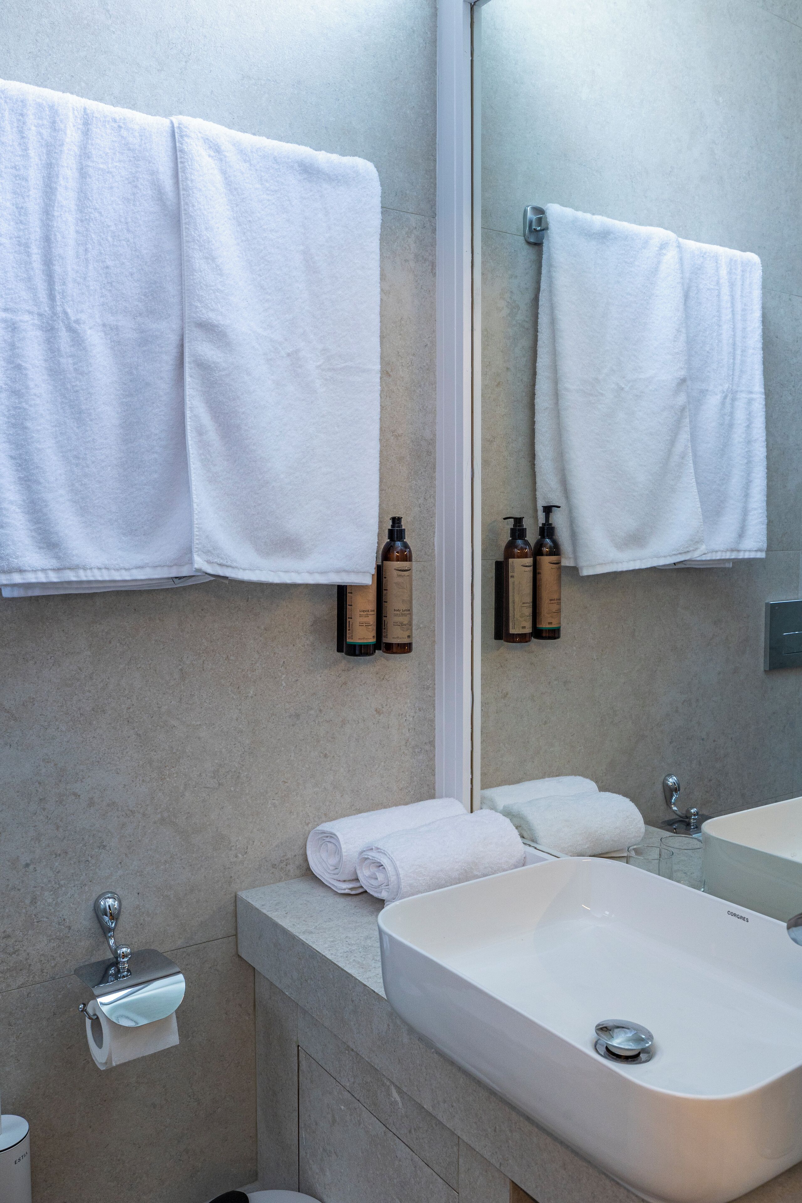 Une salle de bain moderne avec un grand miroir, deux lavabos et un porte-serviettes où sont pliées des serviettes.