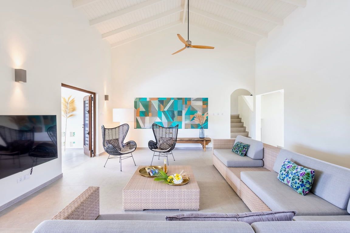 A spacious living room with a high ceiling, a ceiling fan, a large abstract painting, a sofa set, and a coffee table with decorative items.