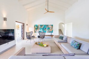 A spacious living room with a high ceiling, a ceiling fan, a large abstract painting, a sofa set, and a coffee table with decorative items. - Stylish retreat with tropical garden and pool (Sint Willibrordus)