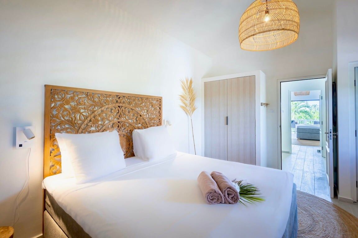 A hotel room with a large bed, a decorative headboard, a bedside lamp, and a view of the outdoor area.
