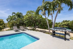 A swimming pool with lounge chairs and a barbecue grill. - Stylish retreat with tropical garden and pool (Sint Willibrordus)