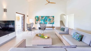 Un salon spacieux avec un plafond haut, un ventilateur de plafond, un grand tableau abstrait, un ensemble de canapés et une table basse agrémentée d’objets décoratifs.