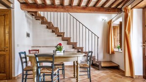 A dining area with a wooden table and chairs, a staircase, and a window with curtains. - Villa of approximately 150 m2 located on the ground floor and on two levels with air conditioning, independent heating and wi fi line.Composed of a large living room with independent equipped kitchen, fridge, microwave oven, toaster, sofa and satellite t (Sorano)