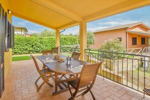 Un patio cubierto al aire libre con una mesa y sillas de madera, un jardín pequeño y vistas a casas vecinas.