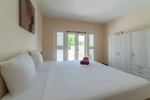 Une chambre à coucher avec un lit, des murs blancs, une porte avec des volets et une armoire.
