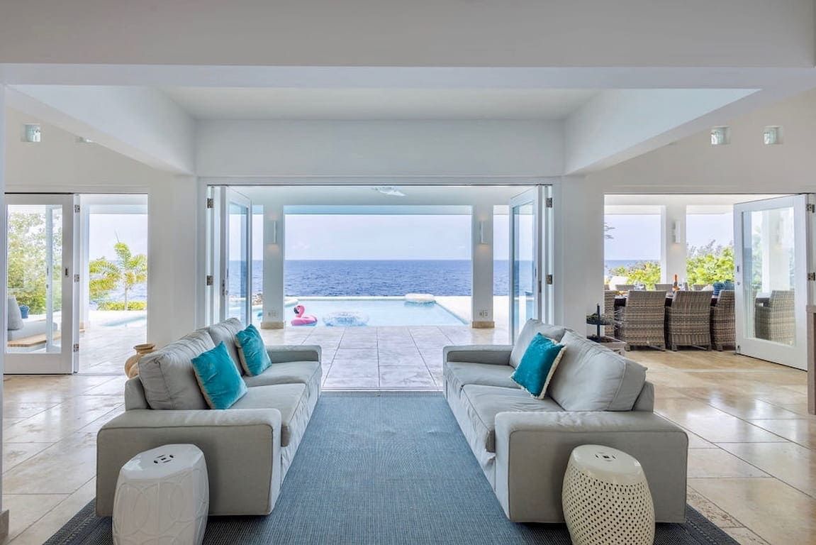 A spacious living area with a view of the sea, two sofas with cushions, a coffee table, and a patterned rug.