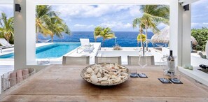 A poolside area with a view of the ocean, a table with a bowl of seashells, and lounge chairs. - Beachfront villa with private beach and pool (Sint Willibrordus)