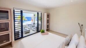 Een slaapkamer met een groot bed, een schuifdeur naar een balkon en uitzicht op de oceaan.