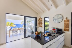 A modern kitchen with a large island, a dining area with a view of the ocean, and a clock on the wall. - Beachfront villa with private beach and pool (Sint Willibrordus)