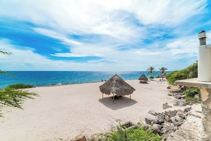 A beach with thatched umbrellas and palm trees, a clear sky, and a calm sea. - Spacious villa with infinity pool and ocean view (Sint Willibrordus)