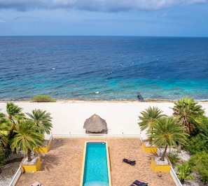 Blick auf einen Strand mit Pool, Palmen und einer Reetdachhütte.