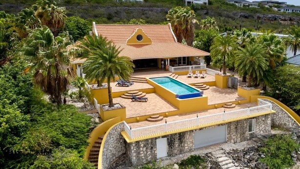 Uma casa costeira com piscina, cercada por palmeiras e um muro de pedra.