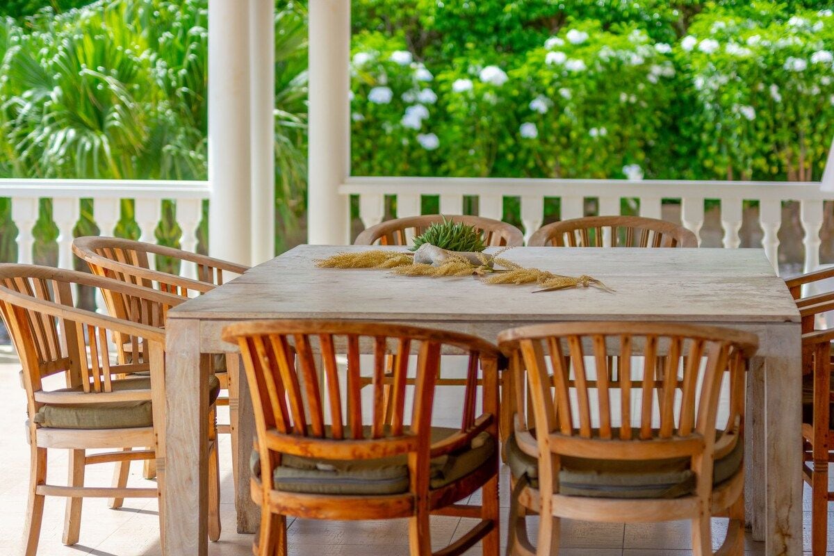 A wooden table with chairs, surrounded by lush greenery.