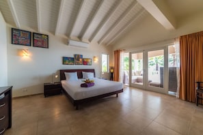 A bedroom with a large bed, a nightstand, a desk, and a window with curtains. - Spacious villa with infinity pool and ocean view (Sint Willibrordus)