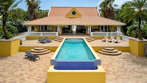 A two-story building with a swimming pool, sun loungers, and a covered patio area. - Spacious villa with infinity pool and ocean view (Sint Willibrordus)