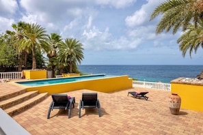 Ein Poolbereich mit Blick auf das Meer, Palmen und eine gelbe Wand.