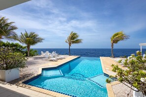 Une piscine avec vue sur l’océan, entourée de palmiers et de chaises longues.