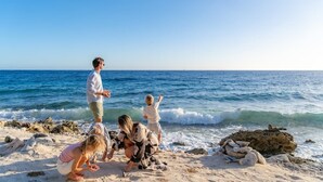 Uma cena de praia com uma família de quatro pessoas, incluindo duas crianças, brincando perto da água.