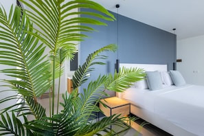 A modern bedroom with a white bed, blue accent wall, and large green plants. - Luxury villa with private beach and sea view (Sint Willibrordus)