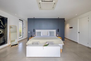 A modern bedroom with a large bed, a bedside table, a mirror, and a large window with blinds. - Luxury villa with private beach and sea view (Sint Willibrordus)