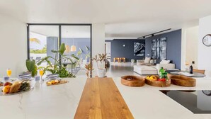 Cozinha moderna com bancada de madeira, sala de jantar com mesa branca e sala de estar com sofá e mesa de centro.