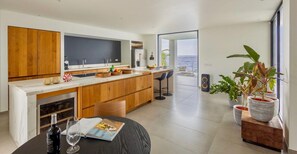 A modern kitchen with wooden cabinets, a marble countertop, and a dining area with a table and chairs. - Luxury villa with private beach and sea view (Sint Willibrordus)