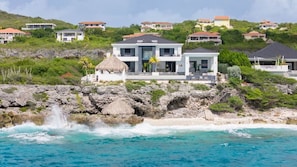A coastal property with a large house, a thatched-roof structure, and a rocky shoreline. - Luxury villa with private beach and sea view (Sint Willibrordus)