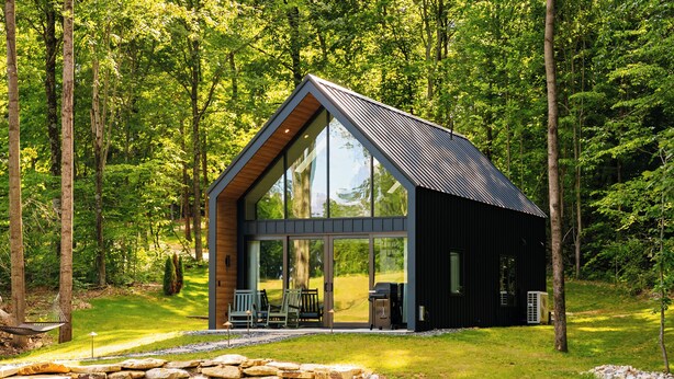 A cabin with a large glass window, a stone pathway, and a pond.