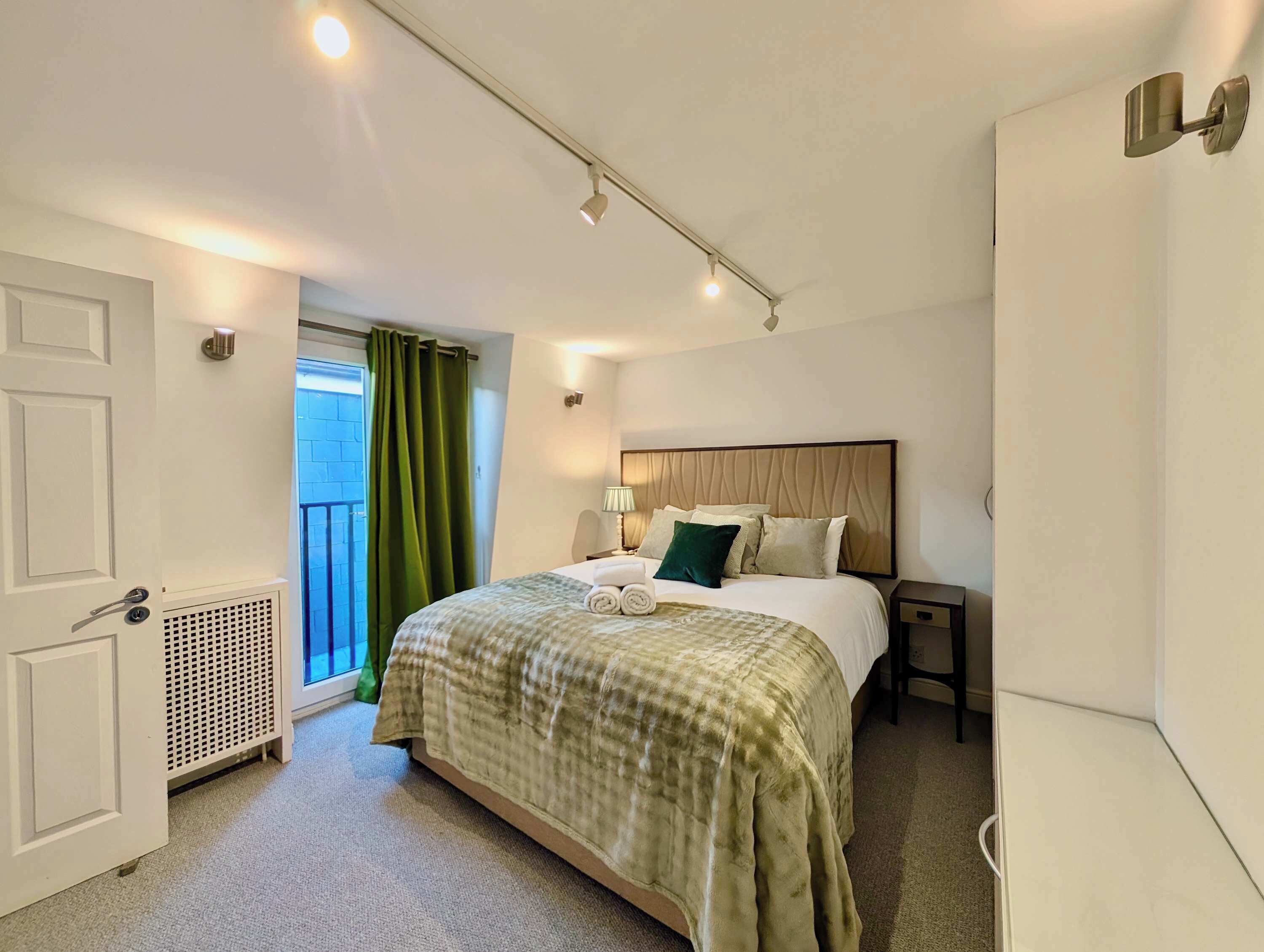 A hotel room with a bed, a nightstand, a lamp, a window with curtains, and a door.