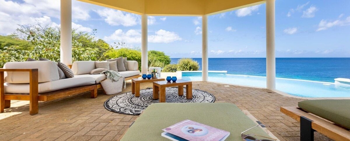 A covered outdoor seating area with a pool and ocean view.
