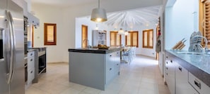 A modern kitchen with a central island, stainless steel appliances, and a dining area with a view. - Oceanfront villa - infinity pool and private beach (Sint Willibrordus)