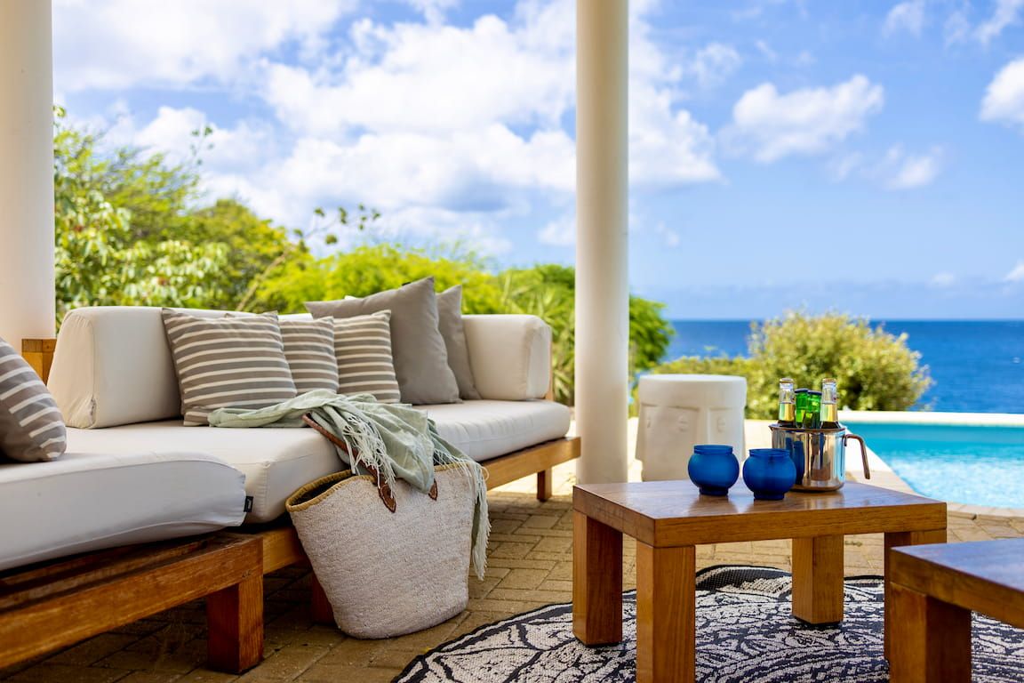 A cozy outdoor seating area with a sofa, a wooden table, and a view of the ocean.